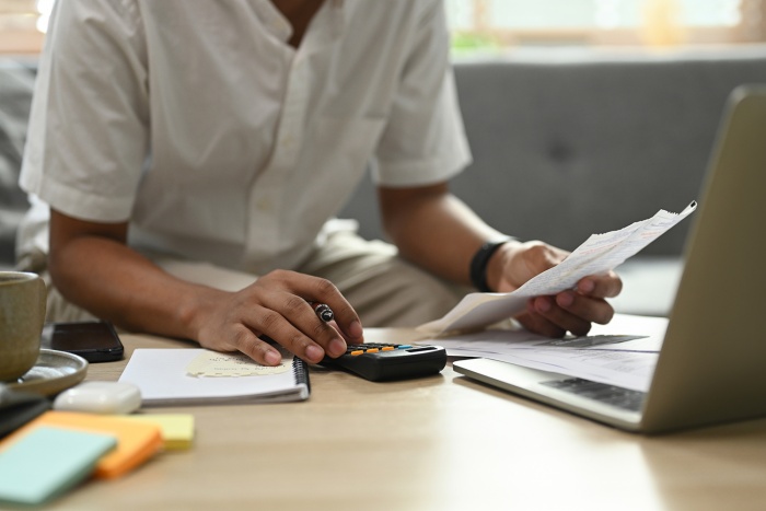 A man uses a calculator and laptop to pay his bills.