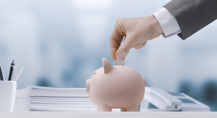 A business man's hand inserts a coin into a piggy bank.