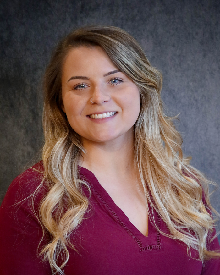 Emily Osmer, a mortgage originator, smiles for a photo, her hair draped over her shoulders, wearing a maroon blouse.