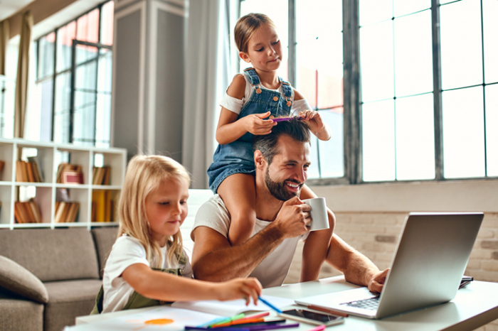 Dad using laptop while daughters play nearby