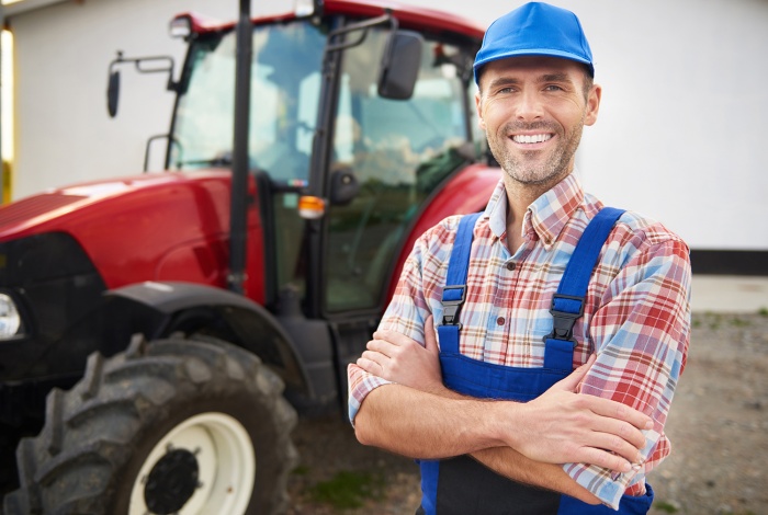 A farmer stands happily in a field next to his tractor