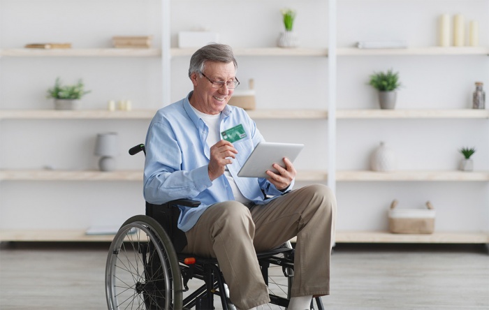 A man in a wheelchair holds his Emerald Visa card in one hand and a tablet in the other.