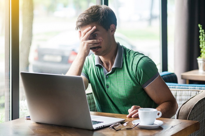 A man blocks his eyes while using his laptop at a café