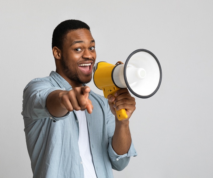 A man smiles and points at the camera using a megaphone