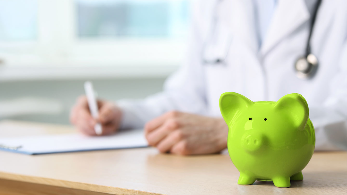 Doctor writing notes with piggy bank on table