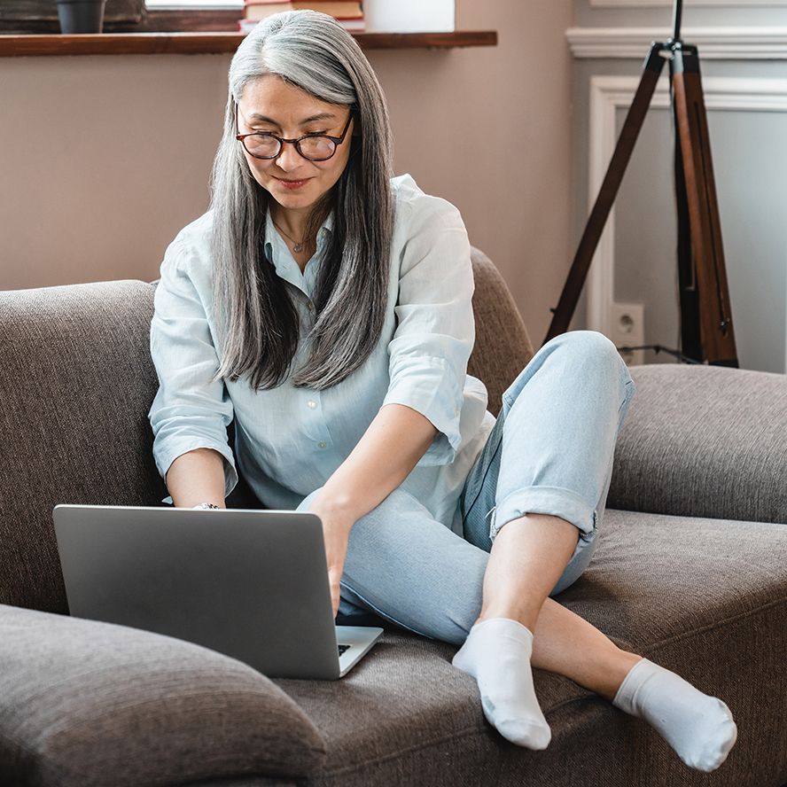 A retiree works on her laptop from her couch